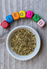 Oregano in Schale mit Buchstabenwürfel auf Holzuntergrund