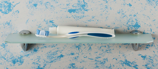 Manual toothbrush and toothpaste lying on glass shelf