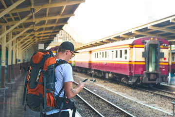 Man with a backpack waiting the train with smart phone in his hand