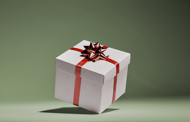 White cube gift box with red stripes and bow floating in intimate green background