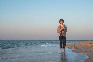 Joyful woman is walking along the beach with the camera
