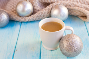 Obraz na płótnie Canvas New Year's silver balls on a blue wooden background with a cup of hot tea or coffee and with a knitted scarf