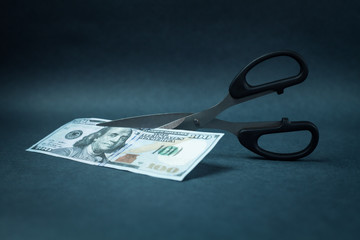 Scissors cutting a hundred dollar on a blue background.
