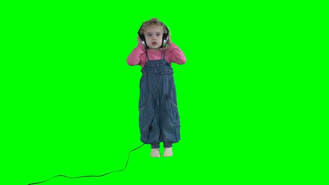 Toddler girl with huge headphones listening for music on green background