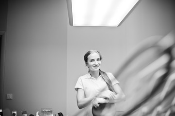 Good-looking female dentist posing in white coat in a modern well-equipped cabinet. Black and white photo.