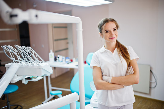 Good-looking female dentist posing in white coat in a modern well-equipped cabinet.
