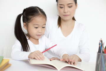 Attractive Little Girl writing Book. Mom Teaching her at home. Children Lifestyle, Education Concept.