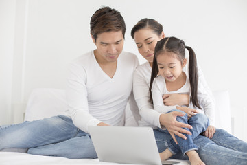 Fototapeta premium Attractive Little Girl using Laptop with Mom and Dad Together. Girl learning to use Laptop. Happy Family Concept.
