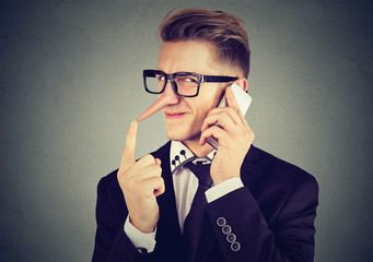 young sly man with long nose talking on mobile phone isolated on gray wall background. Liar...