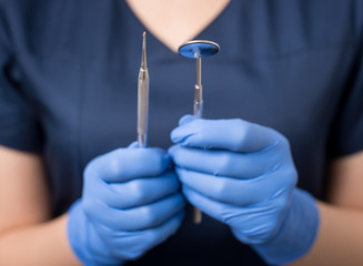 Dentist with blue gloves holding tools - dental mirror and dental probe at the dental office....