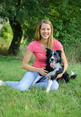 Joyous Woman in Pink Shirt and Blue Jeans Playing with Her White and Black Dog in the Park During Sunny Summer Day Outdoors.