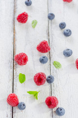 Raspberries and blueberries on white wooden background © eugenaklykova