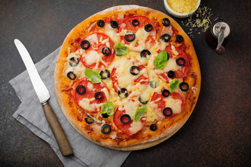 Pizza margarita with tomatoes, mazarella and slices of olives on a dark concrete or stone background. Traditional Italian cuisine. Selective focus. Top view.