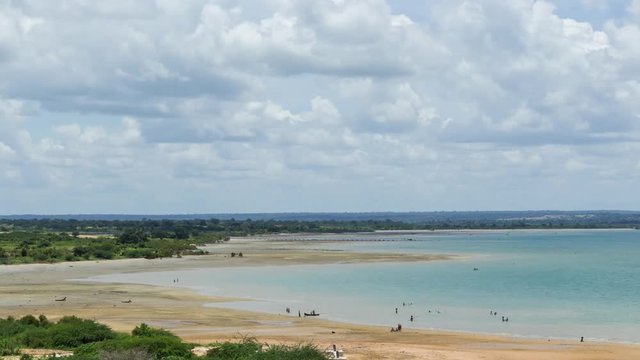 A static longterm timelapse over a few weeks of the ocean tides showing high tide and low tide with communities of people going about at the sea, Mozambique. 