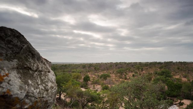 A pan and linear timelapse moving past granitic rock boulders revealing the distant landscape and dry riverbed at sunrise with clouds moving. 