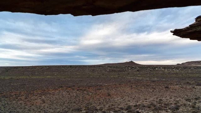 A linear timelapse at twilight framed by rock crevasse with a rocky Karoo landscape and stormy clouds passing over as night falls with dramatic skies. 