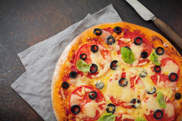 Pizza margarita with tomatoes, mazarella and slices of olives on a dark concrete or stone background. Traditional Italian cuisine. Selective focus. Top view.