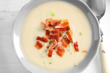 Bowl of yummy potato soup with bacon on wooden table
