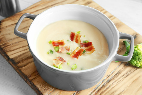 Saucepan of yummy potato soup with bacon on wooden board