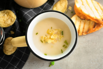Mug of yummy potato soup with crisps on table
