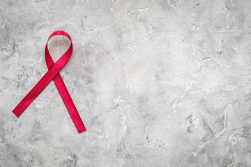 Red ribbon for HIV, AIDS, substance-abuse and anorexia awareness on grey stone background top view copyspace