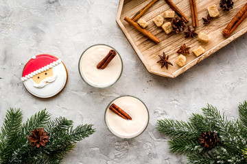 Homemade classic eggnog with cinamon and badian near spruce branch, pinecones, gingerbread on grey stone background top view