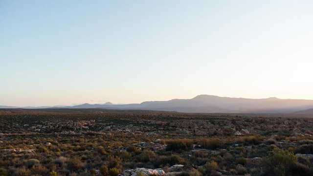 A static day to night timelapse of a rocky landscape with Cederberg Mountains seen from Kaggakamma Nature Reserve as night falls on a moonlit landscape. 