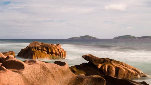 A static early morning timelapse of granitic rocks and waves crashing in the sunlight on La Digue, near Anse Fourmis beach with Felicite and Marianne island in the background. 