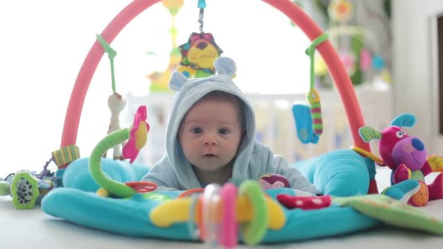 Cute baby boy on colorful gym, playing with hanging toys at home, baby activity and play center for early infant development. Kids playing at home