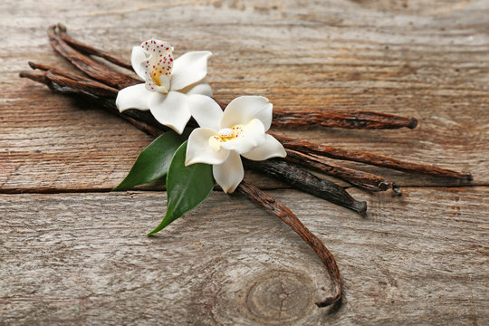 Fototapeta Dried vanilla pods and flowers on wooden background