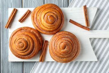 Wooden board with sweet cinnamon rolls on table