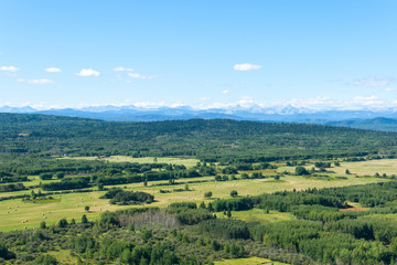Obraz premium Aerial photo of forest and man made farmers fields with Rocky Mountains on the horizon.