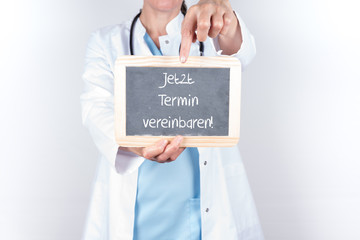 Arzt mit Schild jetzt Termin vereinbaren
