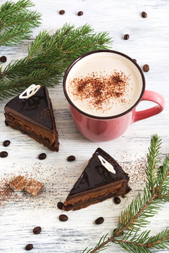 Chocolate cake and coffee with milk on a wooden white table with sprigs of spruce. Christmas photo.
