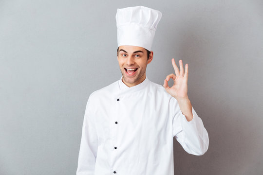 Cheerful young cook in uniform showing okay gesture.