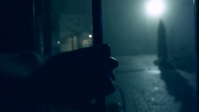 Robber hand touches the fence of private possession at night. Backlight