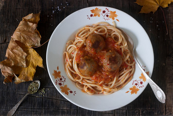 Meatballs in a sauce with pasta on a wooden background with autumn leaves. Rustic style.