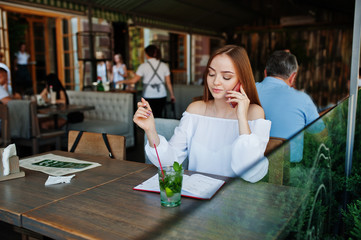 Portrait of a gorgeous young businesswoman talking on the phone and writing something down in her red notebook while sitting in a cafe.