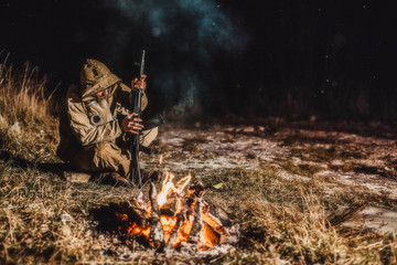 The rebel sits at the night fire and checks the assault rifle