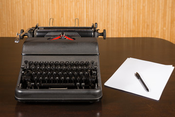 Old typewriter on wooden table with blank paper and pen