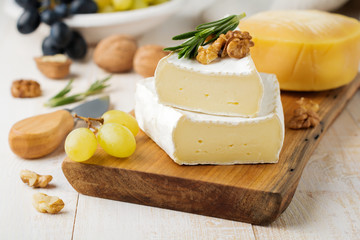 Stack Camembert cheese with grapes, walnuts and basil on gray light concrete or stone background....