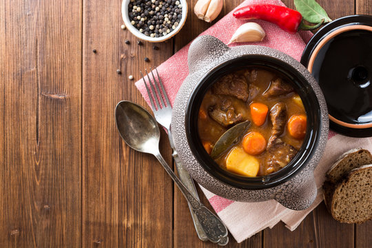 Meat stew with vegetables in ceramic pot on wooden table.