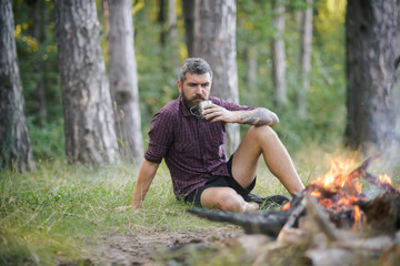 Man traveler drink tea at campfire flame