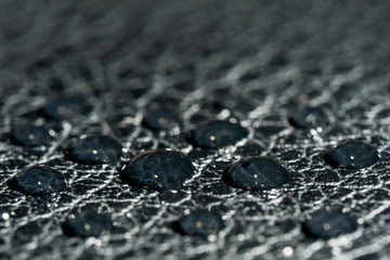dark round drops of water on the embossed surface of black leather, macro background