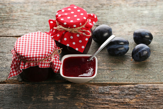 Plum jam in jars with spoon on grey wooden table