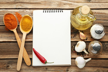 Blank notebook with spices, oil and garlic on wooden table