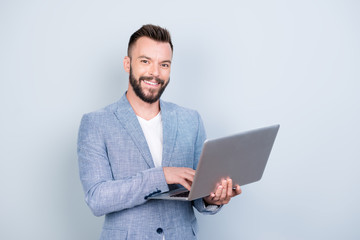 Close up portrait of cheerful brunet bearded business man in formal wear, typing on his laptop, he is a successful lawyer, standing browsing on his device, blue background