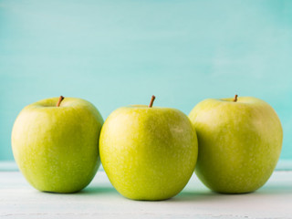 Three Green apples on turquoise background. Healthy food three pillars concept.