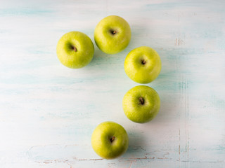 Green apples forming question mark on turquoise white table. Flat lay
