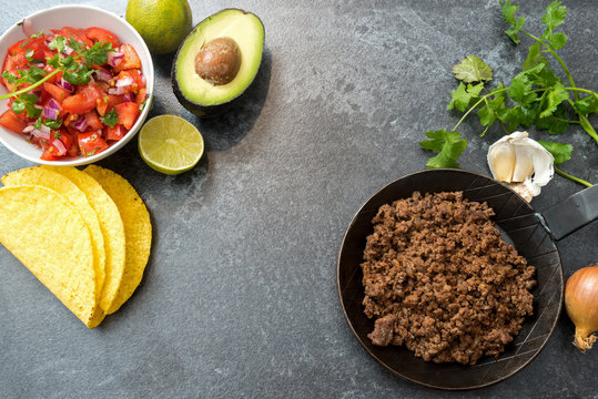 taco ingredients with roasted beef, tomatoe salsa, avocado and herbs on a dark stone background, copy space, top view from above